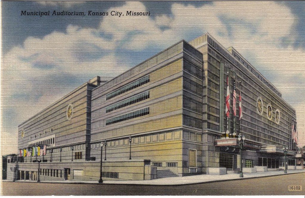 A vintage color postcard of the Municipal Auditorium in Kansas City, a large stone Art Deco building with flags over the entrance