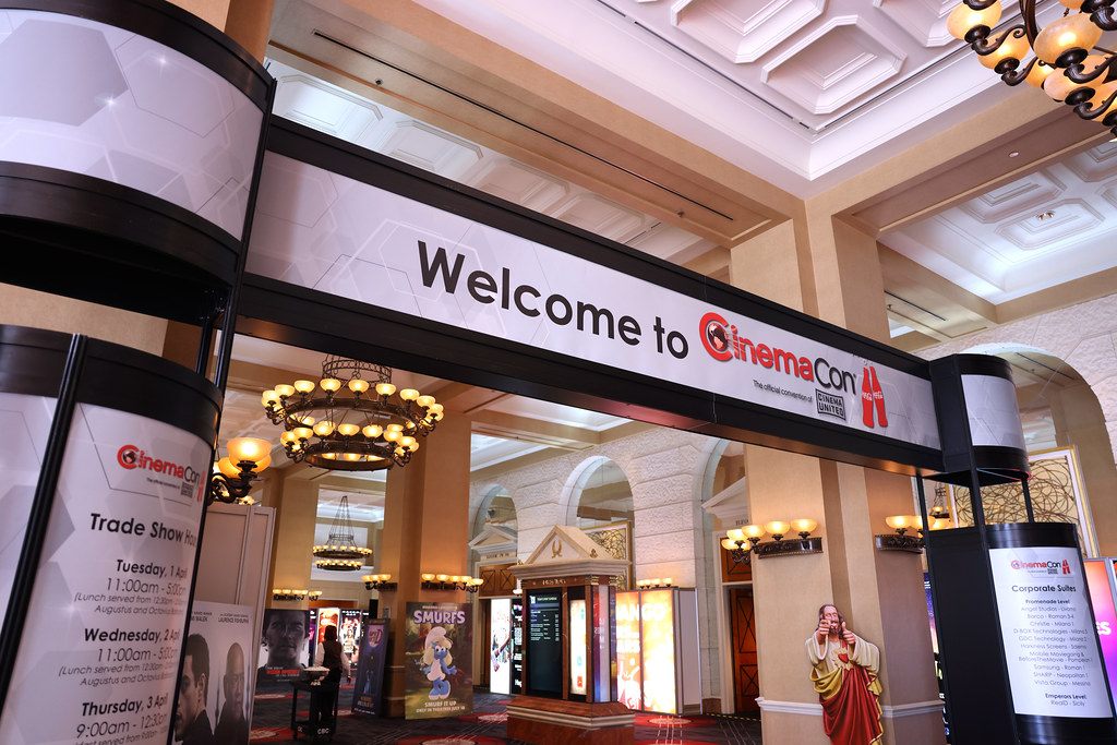 A CinemaCon welcome arch and trade show signs in the chandelier-lit conference corridor at Caesars Palace