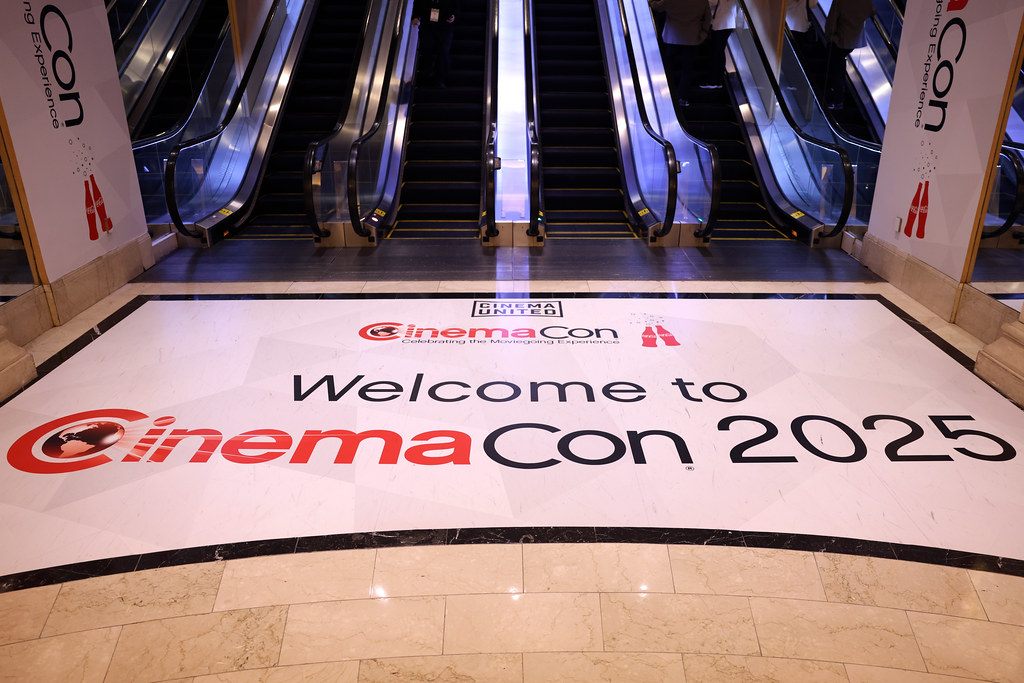A CinemaCon 2025 welcome graphic on the marble floor at the foot of a bank of escalators