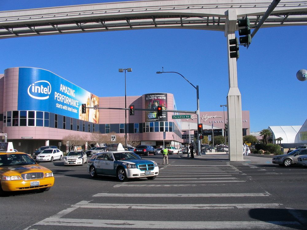 Taxis crossing an intersection under the monorail outside the Las Vegas Convention Center, its walls wrapped in CES advertising