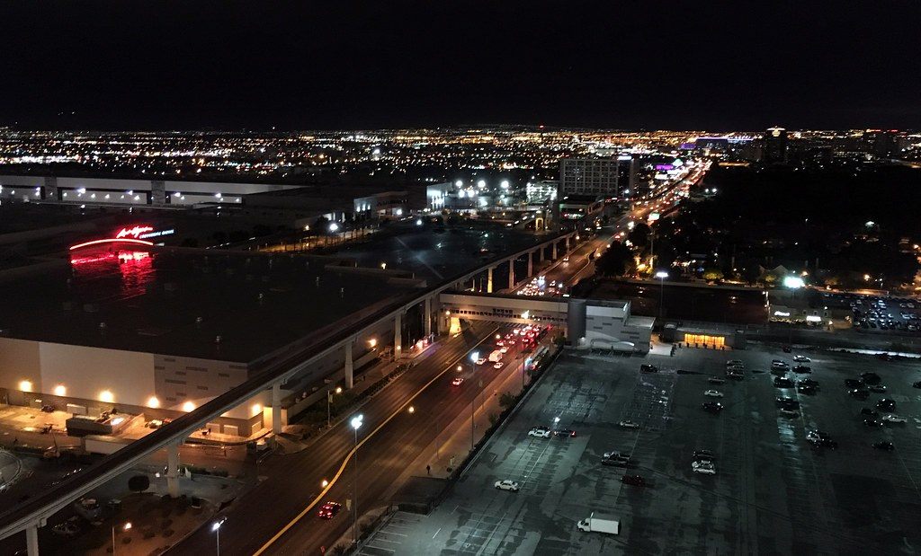 The Las Vegas Convention Center halls and Paradise Road at night, with the elevated monorail track running past the parking lots