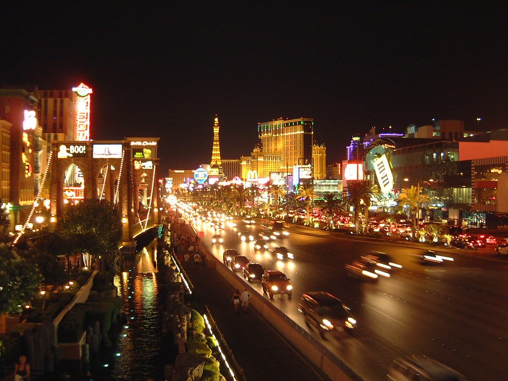 Traffic streaming along Las Vegas Boulevard at night past lit casino signs and palm trees