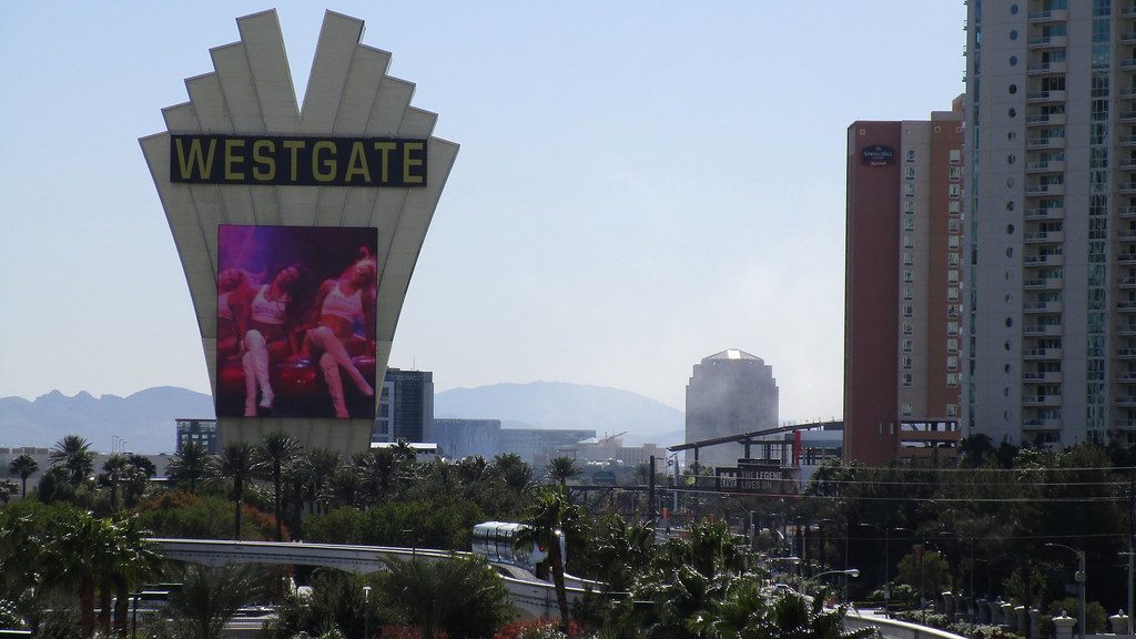 The fan-shaped Westgate sign above palm trees, with a Las Vegas Monorail train on the elevated track at the Westgate station