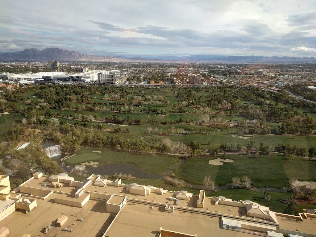 The green fairways and waterfall of the Wynn golf course seen from the hotel tower, with low resort roofs in the foreground