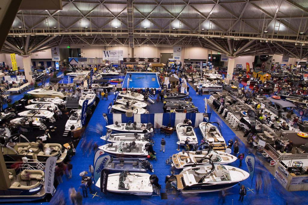 The Minneapolis Boat Show filling an exhibit hall, with a blue display pool in the middle and the hall's steel roof trusses above