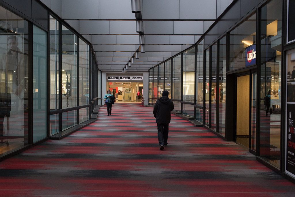 A glass-walled Minneapolis skyway with red and gray carpet and a few people walking