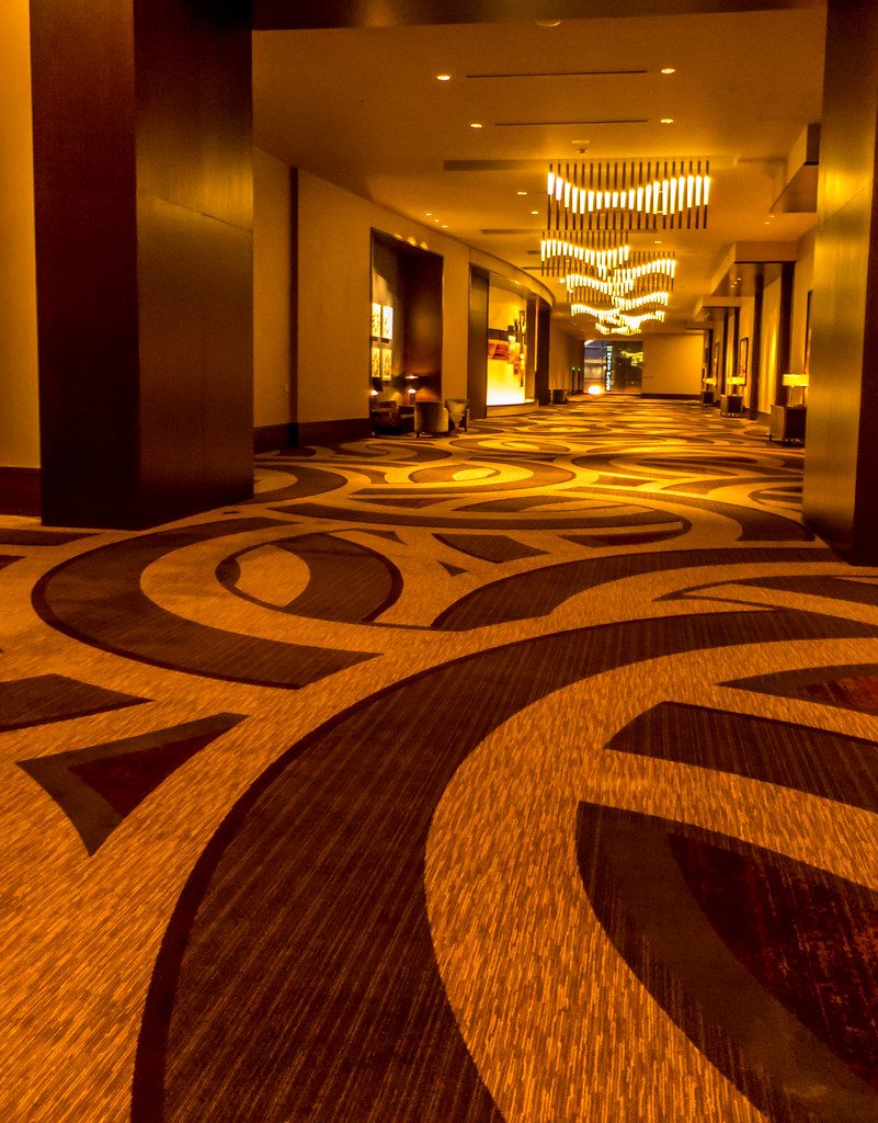 A long prefunction corridor on the Omni Nashville meeting level with swirling patterned carpet and a cascading light-bar chandelier