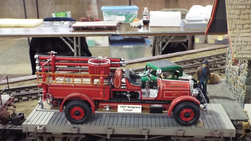 A model 1927 Seagrave fire pumper on a flatcar on a model railroad layout at a fairgrounds train show