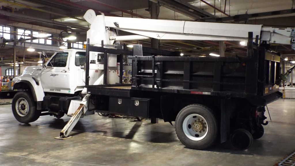A white boom truck parked on the bare concrete floor of a steel-truss fairgrounds hall during a train show