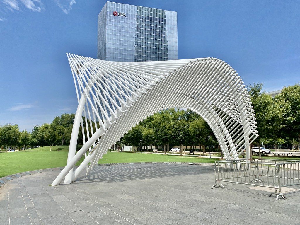 A white ribbed bandshell on the Devon Lawn at Myriad Botanical Gardens, with a glass office tower behind