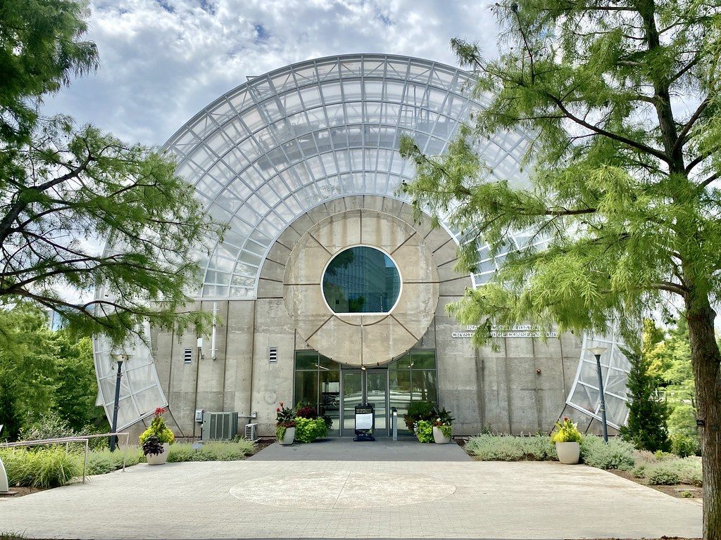 The glass Crystal Bridge Tropical Conservatory at the Myriad Botanical Gardens, framed by trees under a cloudy sky