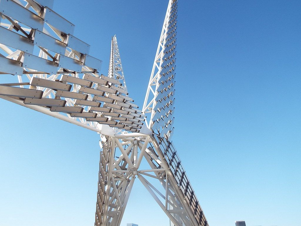 Looking up at the white steel wings of the Skydance Bridge sculpture against a deep blue sky
