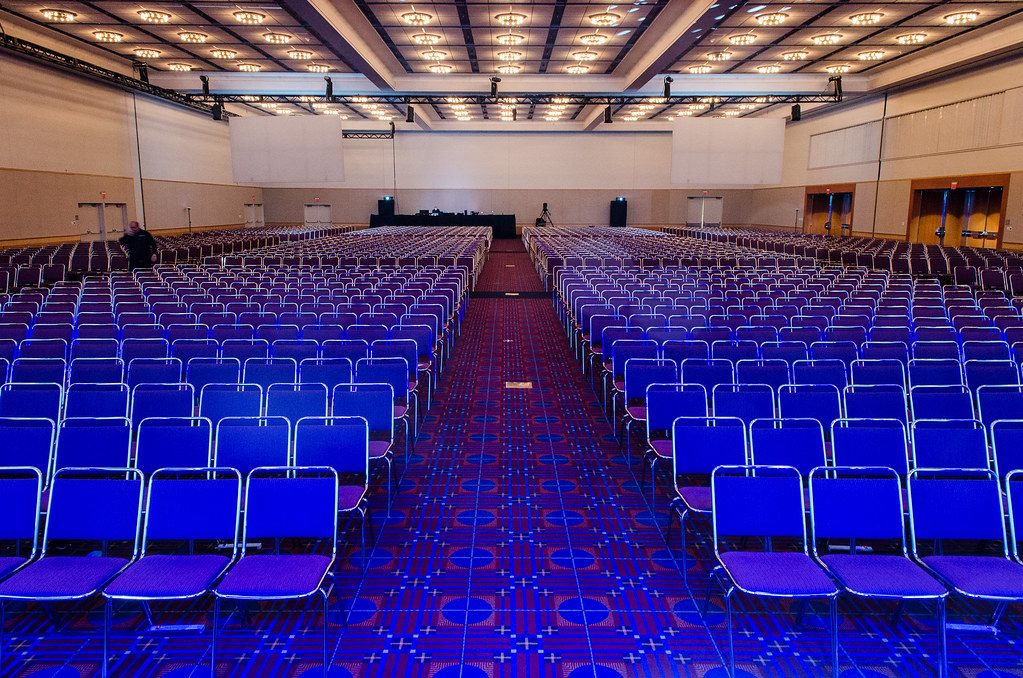 Rows of blue chairs lit in purple filling the Oregon Ballroom before a general session, with a stage at the far end