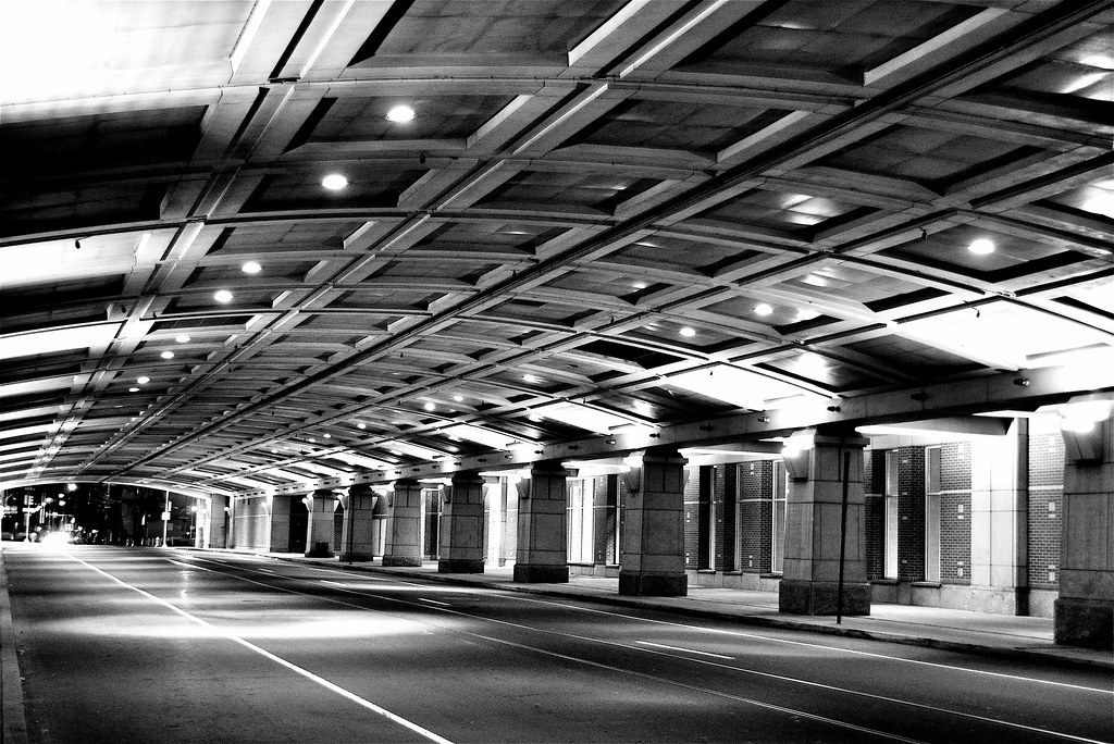 Black-and-white view of an empty street running through a long ribbed tunnel beneath the convention center, lined with stone piers