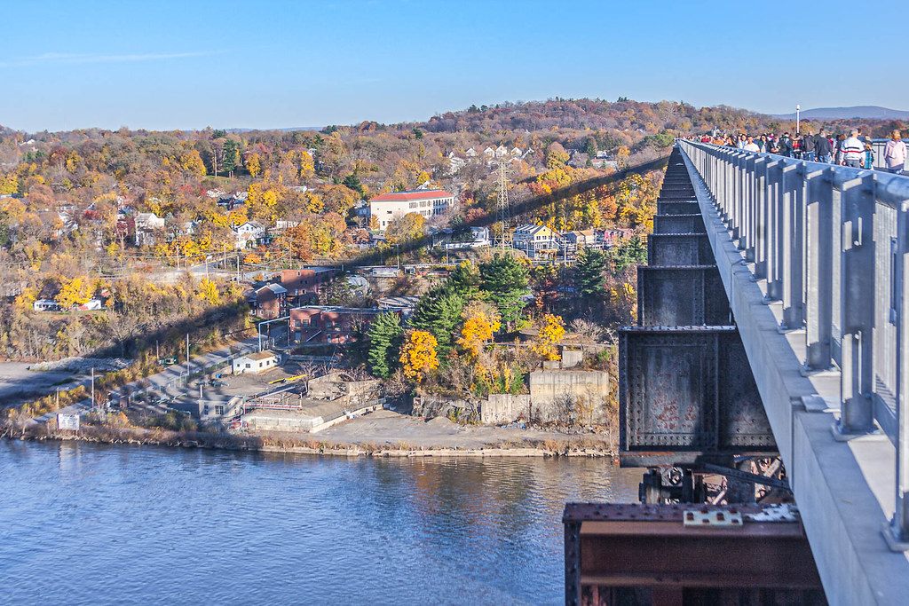 Walkers on the Walkway Over the Hudson high above the river, with autumn trees on the bank below