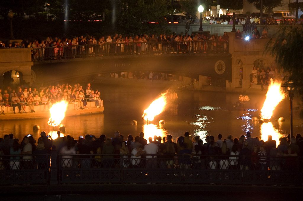 WaterFire braziers burning on the river at night, with crowds on a bridge and along the banks