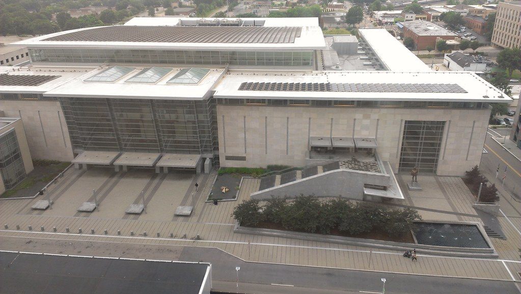 High aerial view of the Raleigh Convention Center's flat roofs, glass corner and stepped stone plaza on Salisbury Street