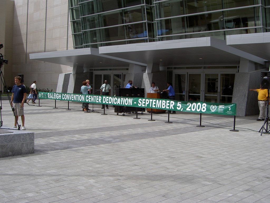 A green banner reading Raleigh Convention Center Dedication September 5, 2008 stretched across the entrance plaza, with a podium and news cameras
