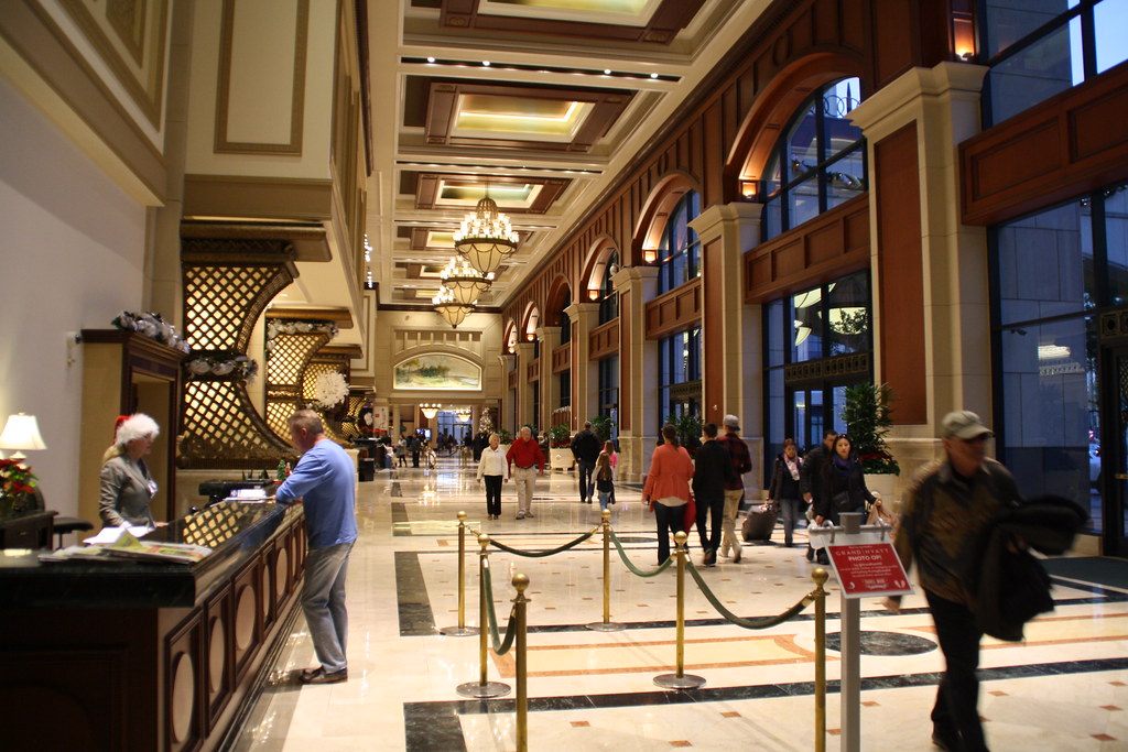 The long marble lobby gallery of the Manchester Grand Hyatt with coffered ceilings, chandeliers, arched windows and guests walking past the front desk