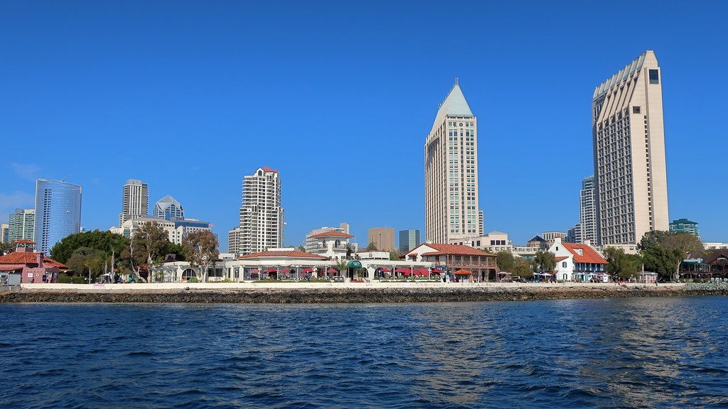 The Manchester Grand Hyatt towers and downtown San Diego high-rises seen across the blue water of San Diego Bay, with Seaport Village along the shore