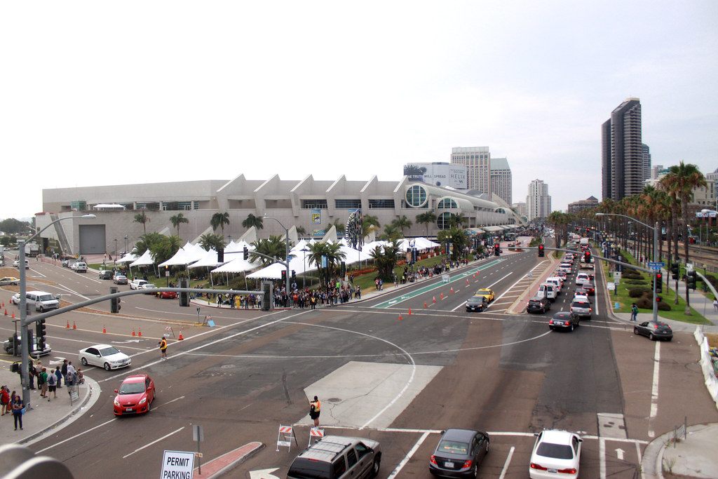 The San Diego Convention Center seen from above on a busy show day, with white tents, crowds on the lawn and traffic on Harbor Drive