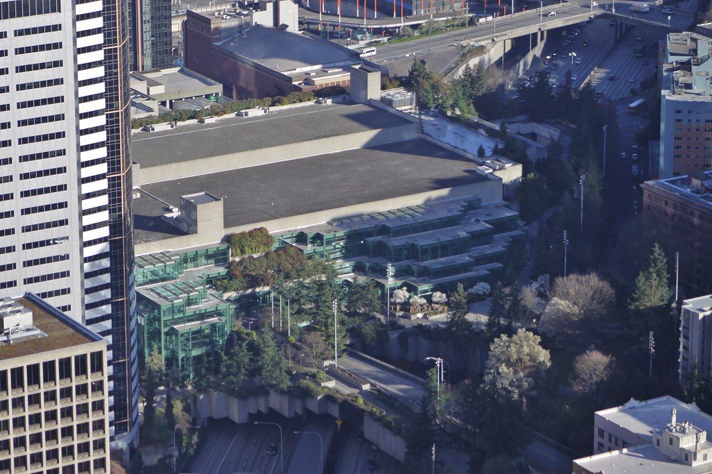 Aerial view of the Arch building's broad roof and green glass facades, with the freeway running alongside and trees of Freeway Park below
