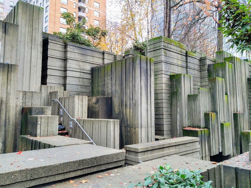 Board-formed concrete terraces and steps in Freeway Park, with autumn leaves and an apartment tower behind