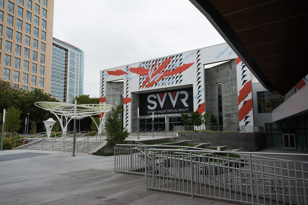 The front of the San Jose McEnery Convention Center with a red and white tile mural, a white canopy sculpture and wide steps, decorated with SVVR signs