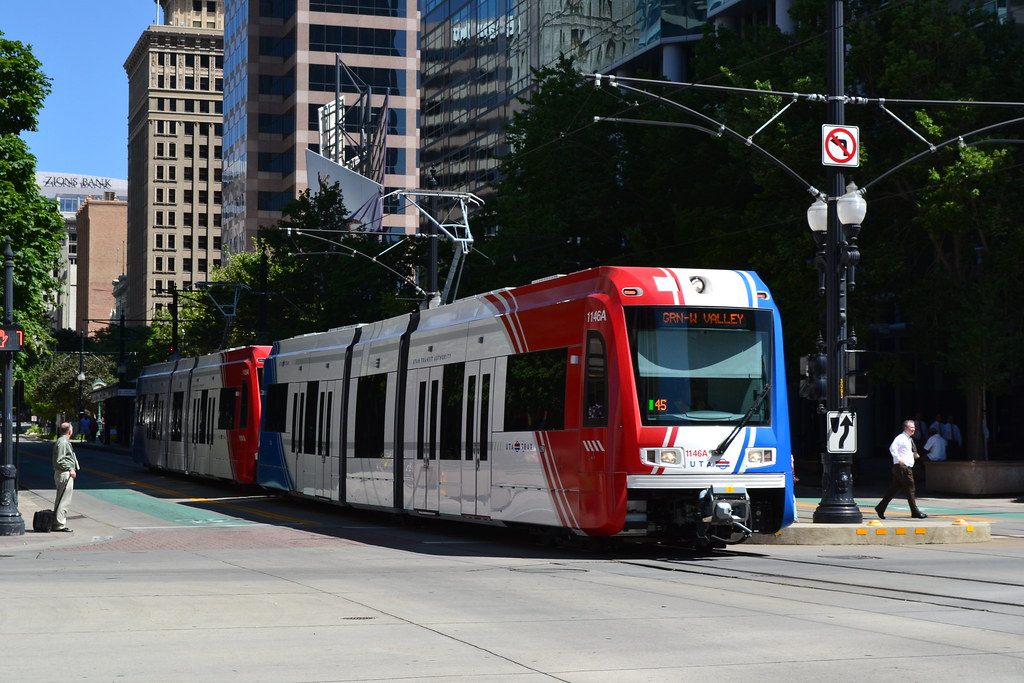 A red, white and blue TRAX light rail train on a downtown Salt Lake City street lined with office towers