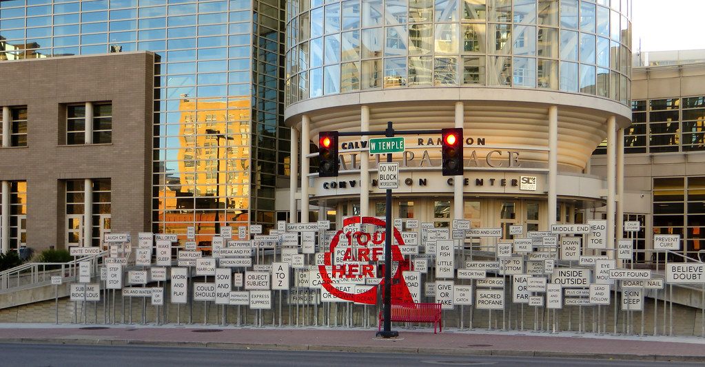 A field of white word signs and a red You Are Here sign in front of the Salt Palace tower entrance on West Temple