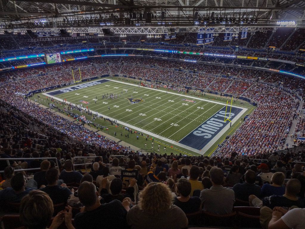 A packed Rams football game on the turf inside the Edward Jones Dome, seen from the upper deck under the roof trusses