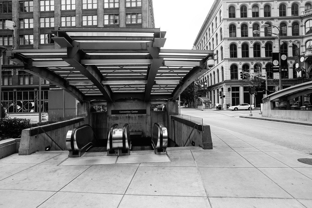 Black and white view of escalators under a steel canopy leading down to the Convention Center MetroLink station on a downtown street