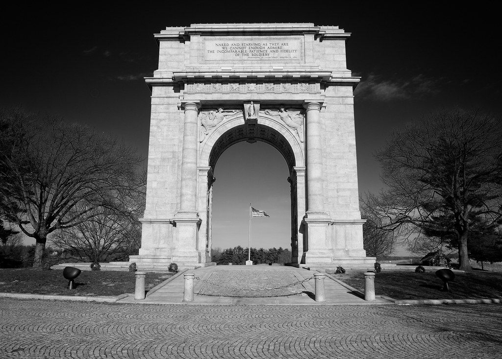 Black-and-white view of the National Memorial Arch in Valley Forge National Historical Park, with an American flag framed in the archway