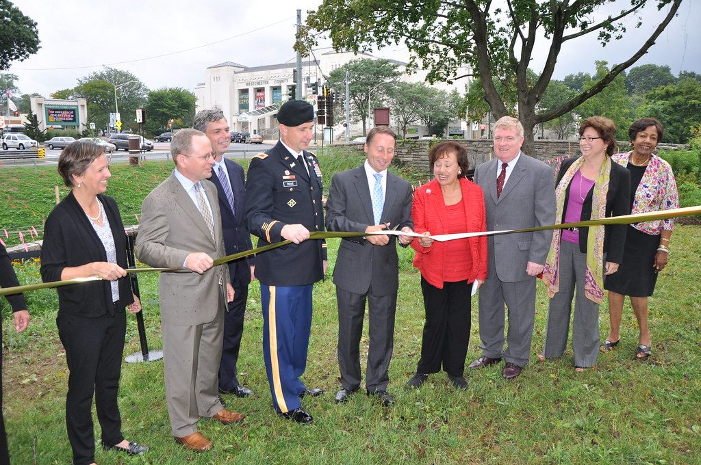 Officials cutting a ribbon on a grassy bank, with the white Westchester County Center building visible behind them across the road
