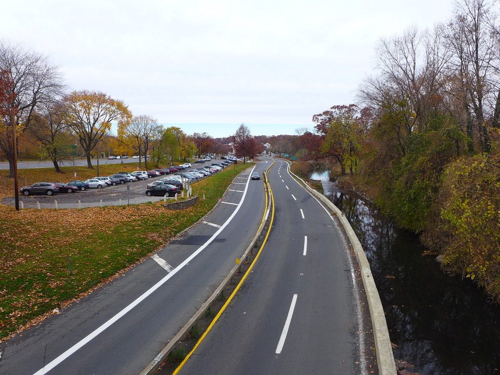 A curving parkway beside a river and a parking lot lined with autumn trees in White Plains