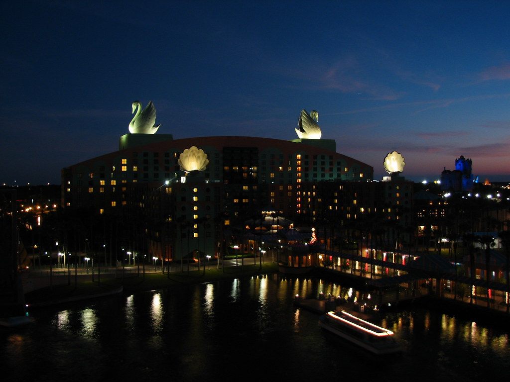 The Swan hotel lit at night with its two glowing swan statues and clamshell fountains on the roof, reflected in the dark water below