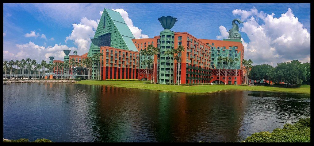 The Dolphin hotel reflected in a lake: a turquoise triangular tower flanked by coral wings, with giant clamshell fountains and a dolphin statue on the roofline