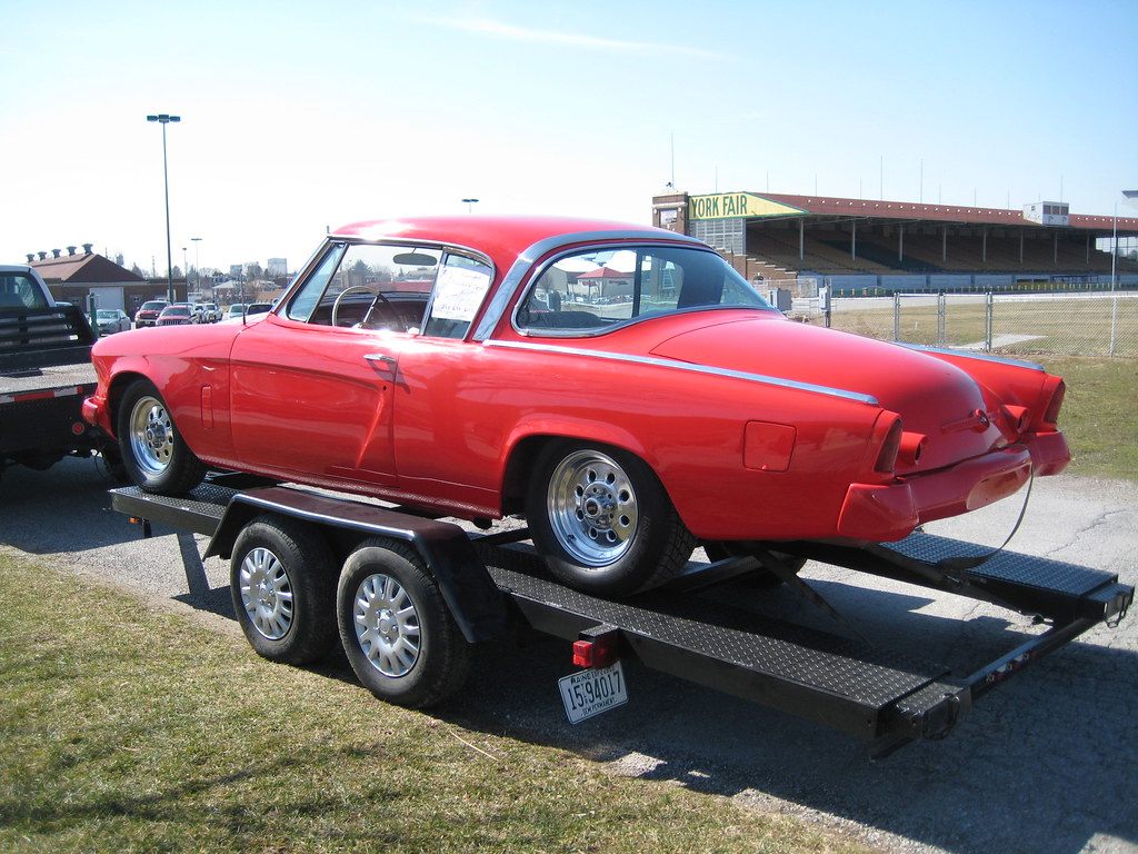 A red Studebaker coupe on a car trailer on the fairgrounds, with the York Fair grandstand and its sign in the background