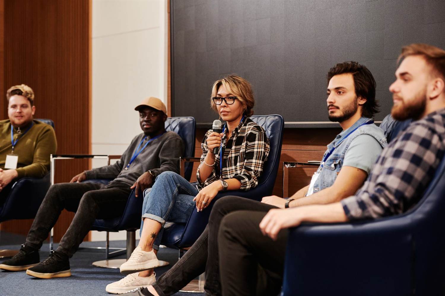 Panel speakers wearing lanyards seated on a conference stage, one holding a microphone