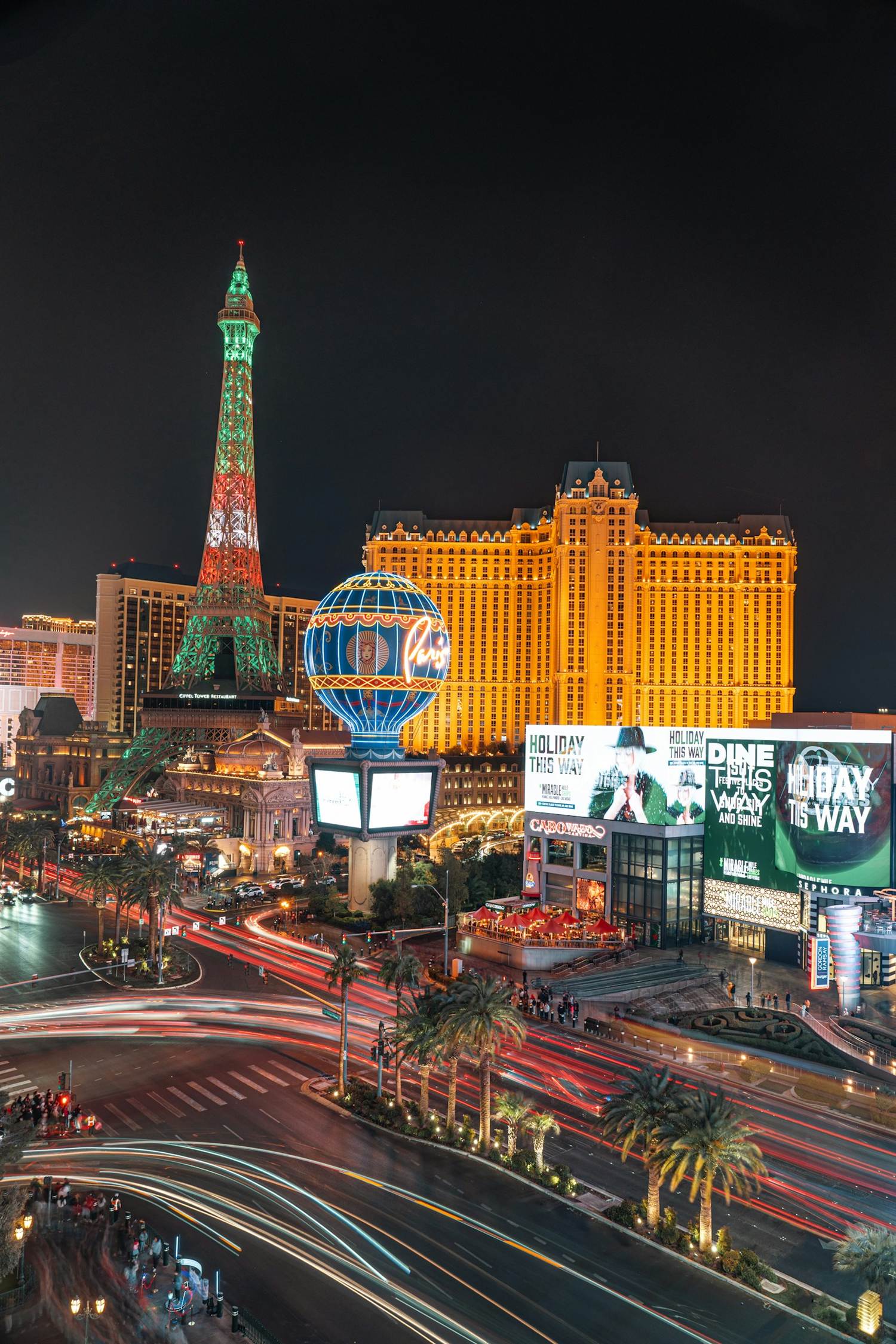 Paris Las Vegas at night with the Eiffel Tower lit in green and red and traffic light trails