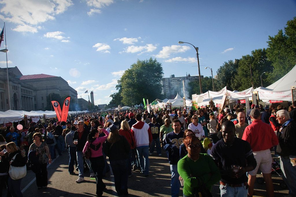 A big crowd strolling between white vendor tents at the Taste of St. Louis food festival on a sunny day