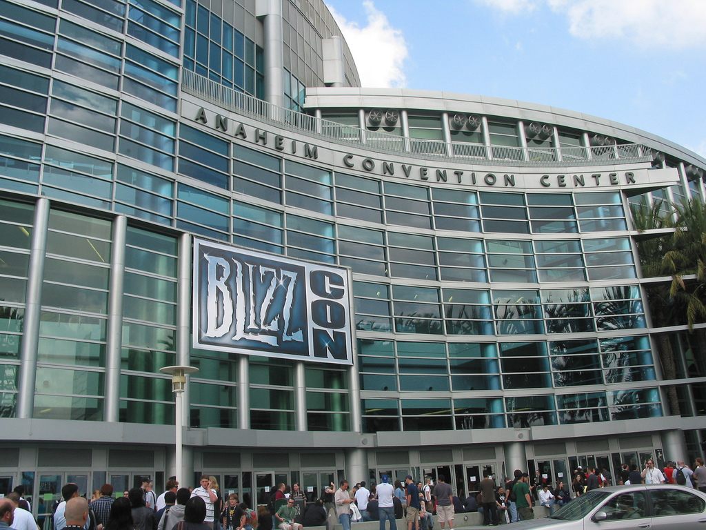 The curved glass facade of the Anaheim Convention Center with its name in large letters and a BlizzCon banner, attendees gathered below