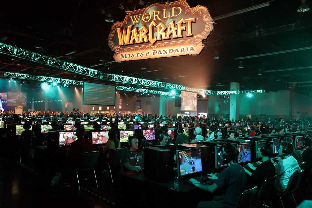 Rows of players at glowing game stations under a World of Warcraft Mists of Pandaria sign and lighting truss in an Anaheim Convention Center hall at BlizzCon 2011