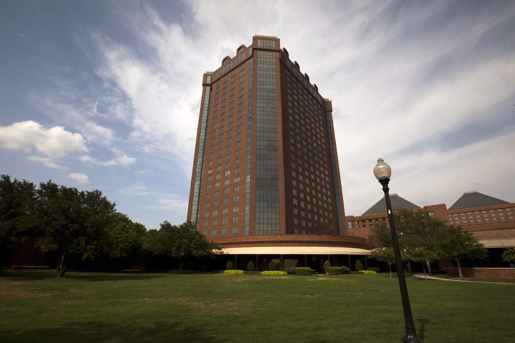 The brick Tower of the Hilton Anatole above a lawn, with the pyramid roofs of the Atrium buildings at right