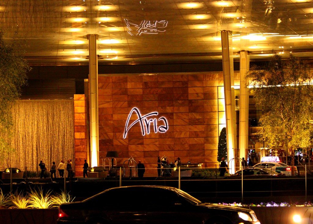 Guests and bell carts under the glowing porte-cochere of the ARIA Resort main entrance at night