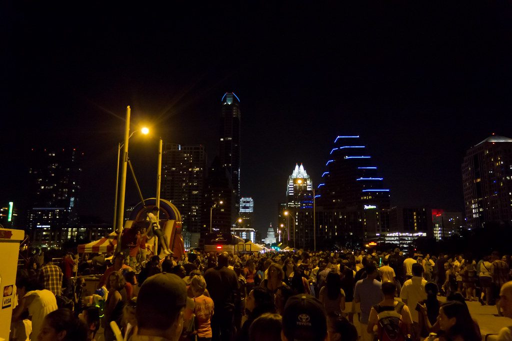 A big nighttime crowd on Congress Avenue near the bridge, with lit downtown Austin towers behind