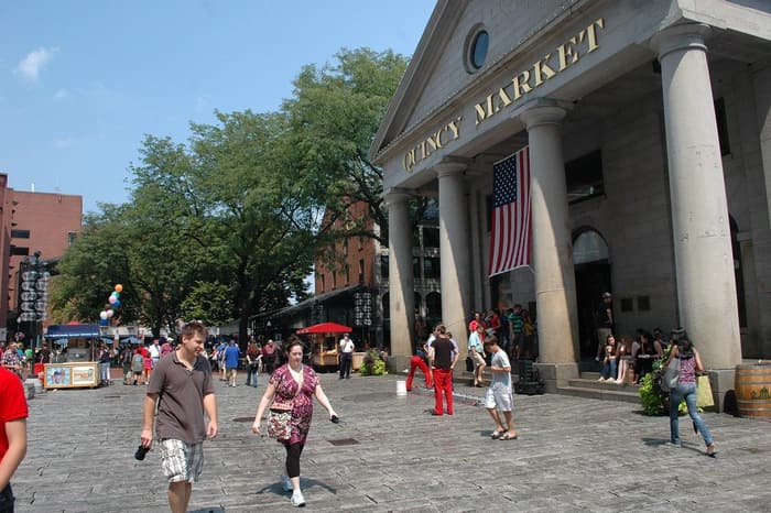 Summer visitors walking the cobblestones in front of the columned Quincy Market building at Faneuil Hall Marketplace in Boston