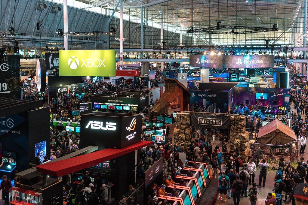 Overhead view of the packed PAX East 2019 show floor at the Boston Convention and Exhibition Center, with Xbox, PlayStation and ASUS booths under the hall's glass and steel roof