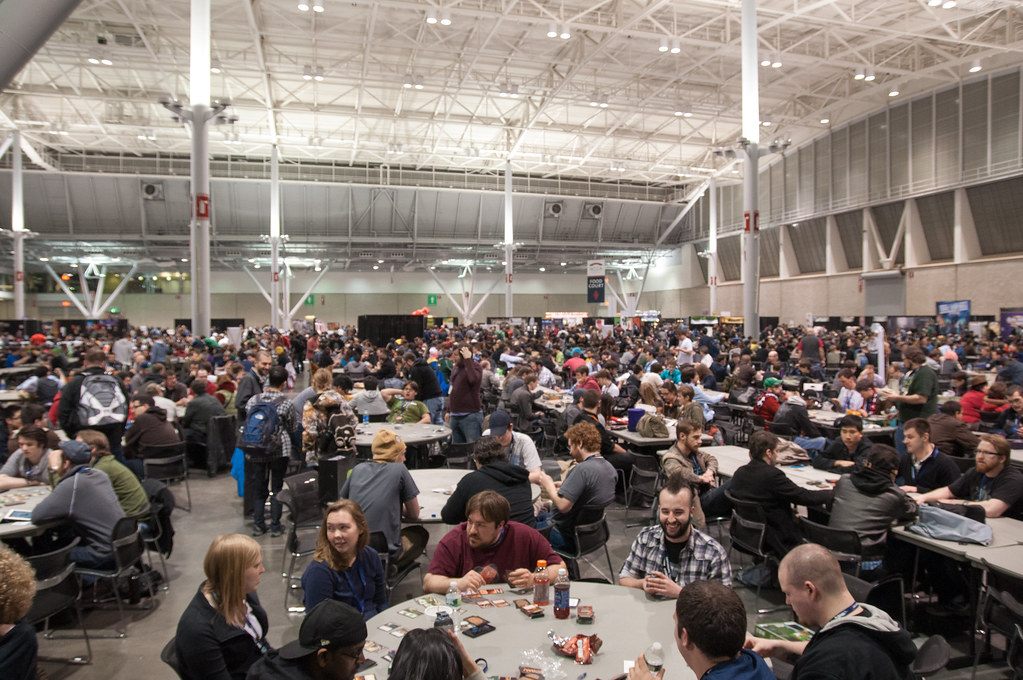 Hundreds of PAX East 2013 players at round tables in the tabletop gaming hall of the Boston Convention and Exhibition Center, under a white steel roof frame