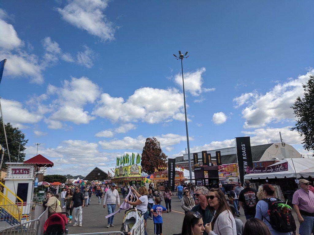Fairgoers crowding a midway lane past ticket booths, game stands and vendor tents at the Big E